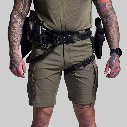 Person wearing tactical shorts and gear with multiple holsters on a plain background