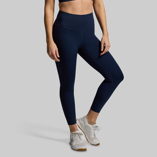 Person wearing navy leggings and white sneakers on a gray background