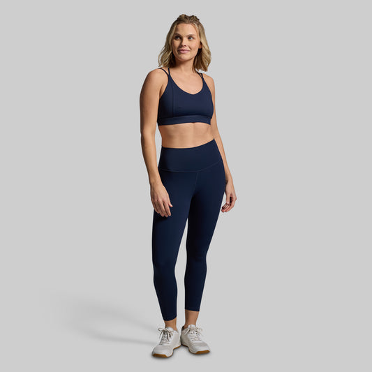 Woman wearing a blue sports bra and leggings on a gray background