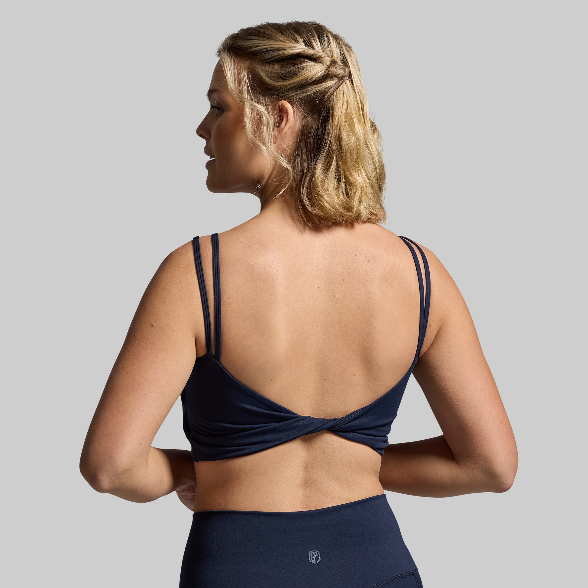 Woman wearing a navy blue sports bra and leggings on a gray background