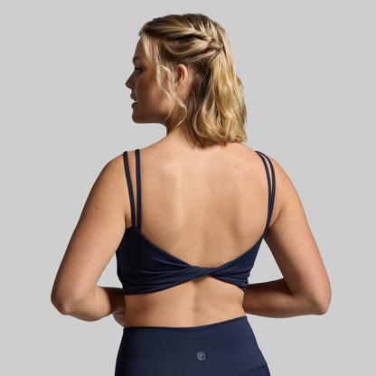 Woman wearing a navy blue sports bra and leggings on a gray background