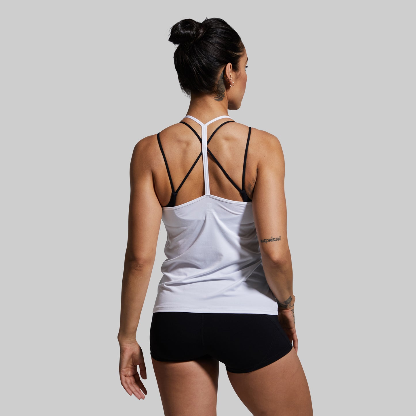 Woman wearing a white tank top with racerback design and black shorts on a gray background