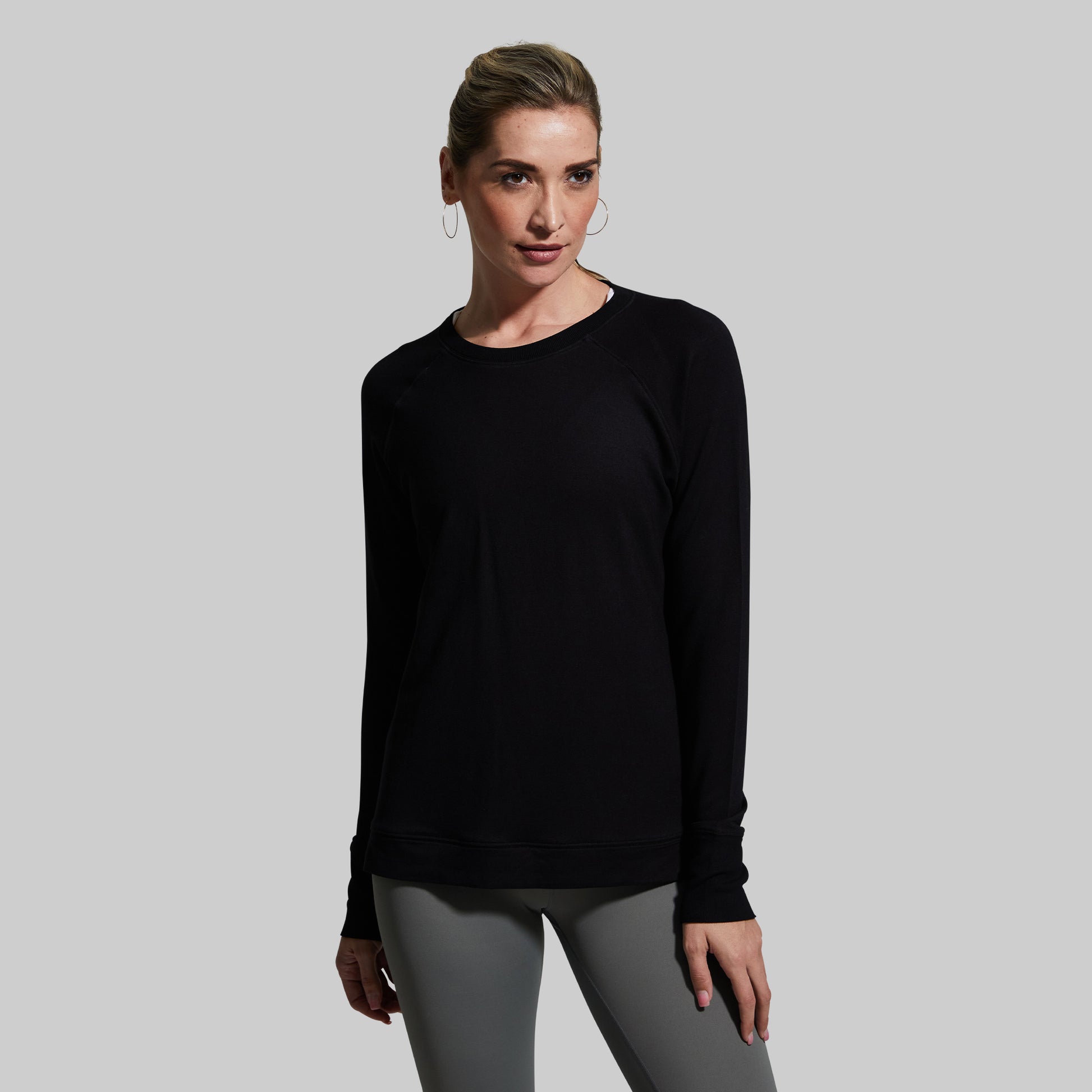 Woman wearing a black long-sleeve top and gray leggings against a plain background