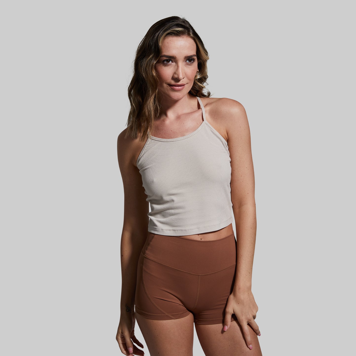 Woman wearing a beige tank top and brown shorts against a plain background