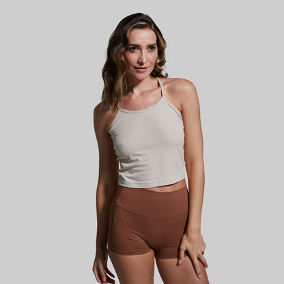 Woman wearing a beige tank top and brown shorts against a plain background