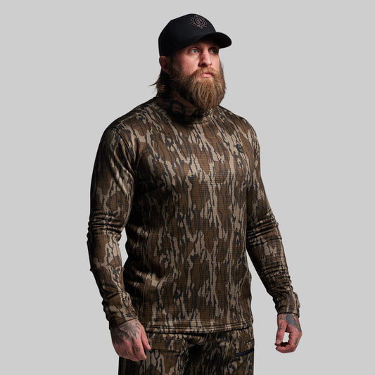 Man wearing a camouflage long-sleeve shirt and pants with a cap on a gray background