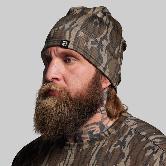Man wearing a camouflage beanie and shirt against a gray background
