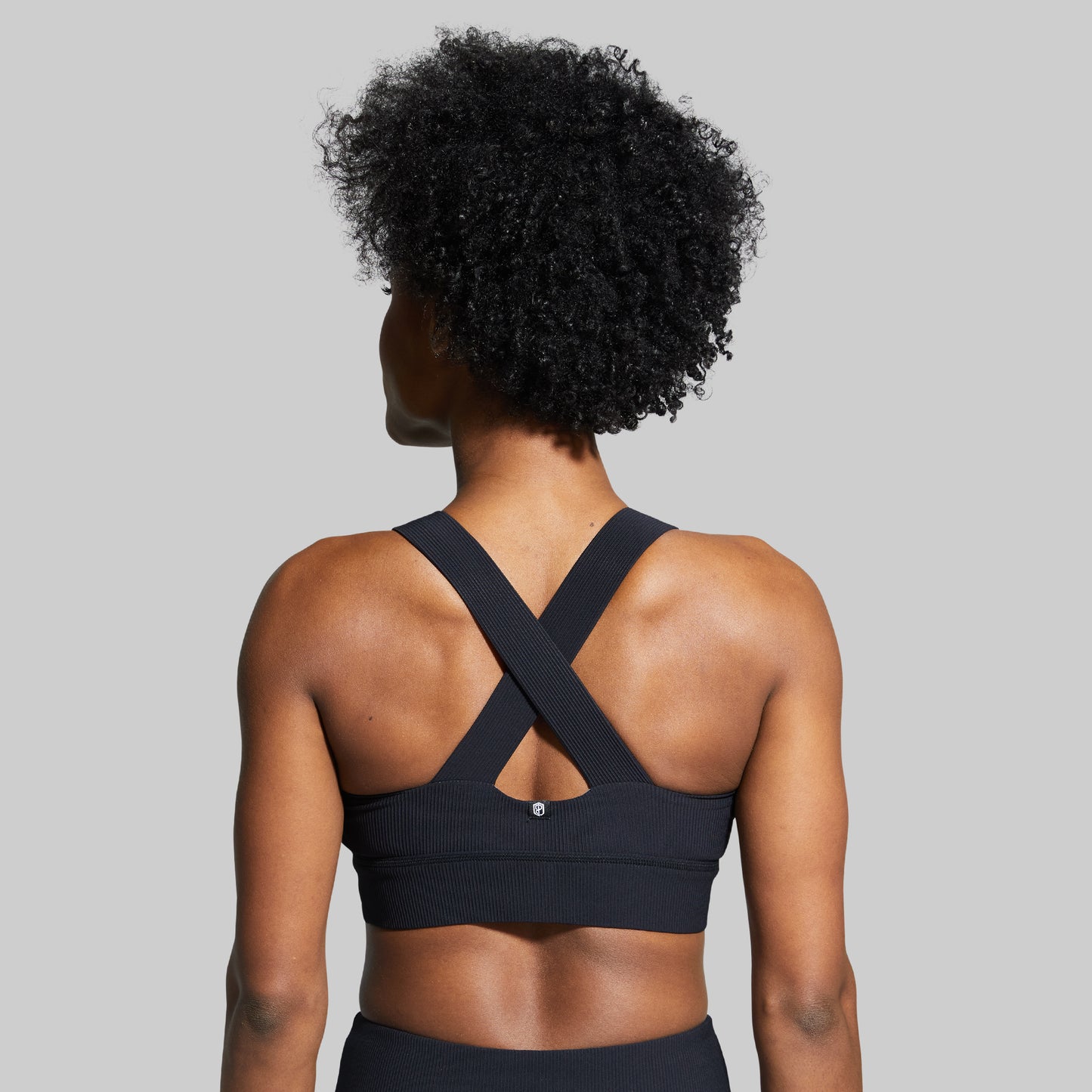 Person wearing a black sports bra with criss-cross straps on a gray background
