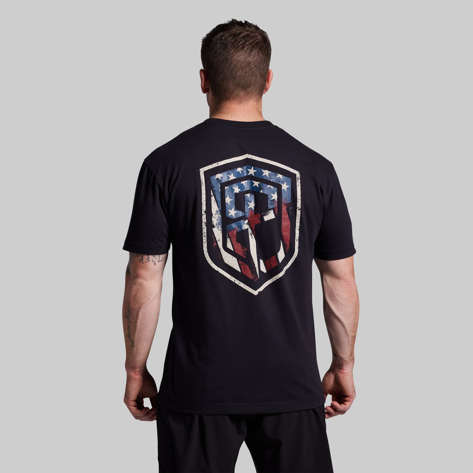 Man wearing a black t-shirt with a shield design on the back against a gray background