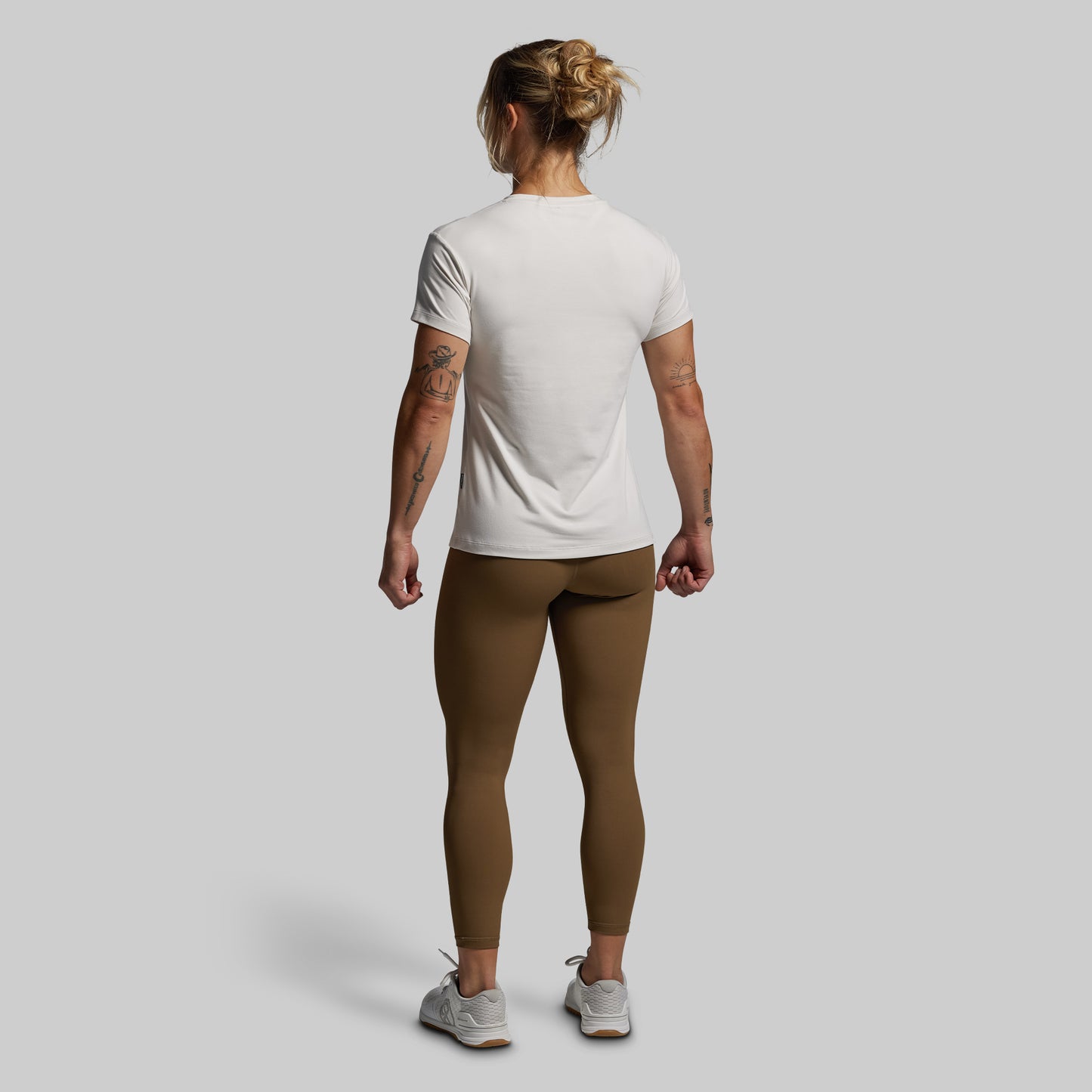 Person wearing a white t-shirt and brown leggings on a plain background
