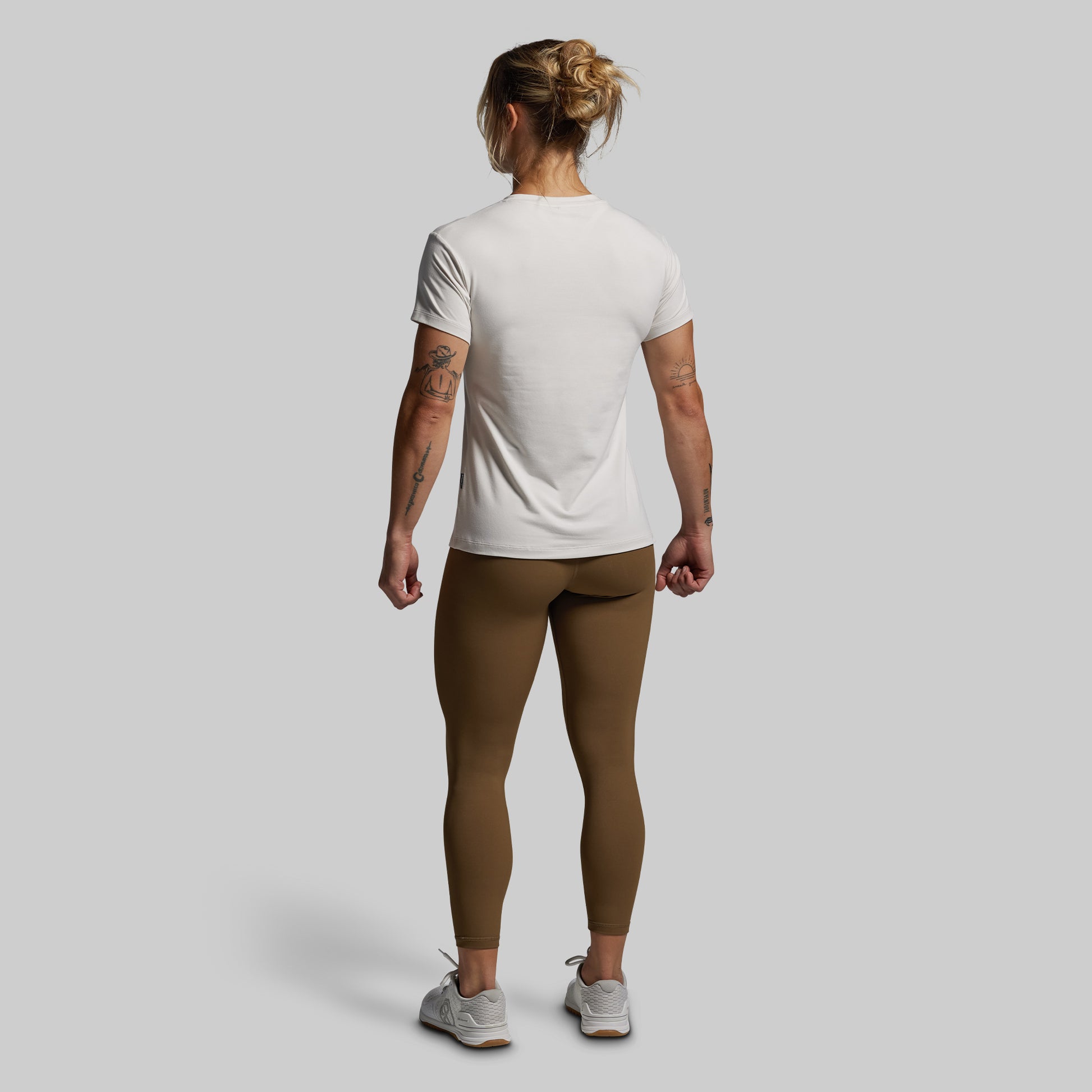 Person wearing a white t-shirt and brown leggings on a plain background