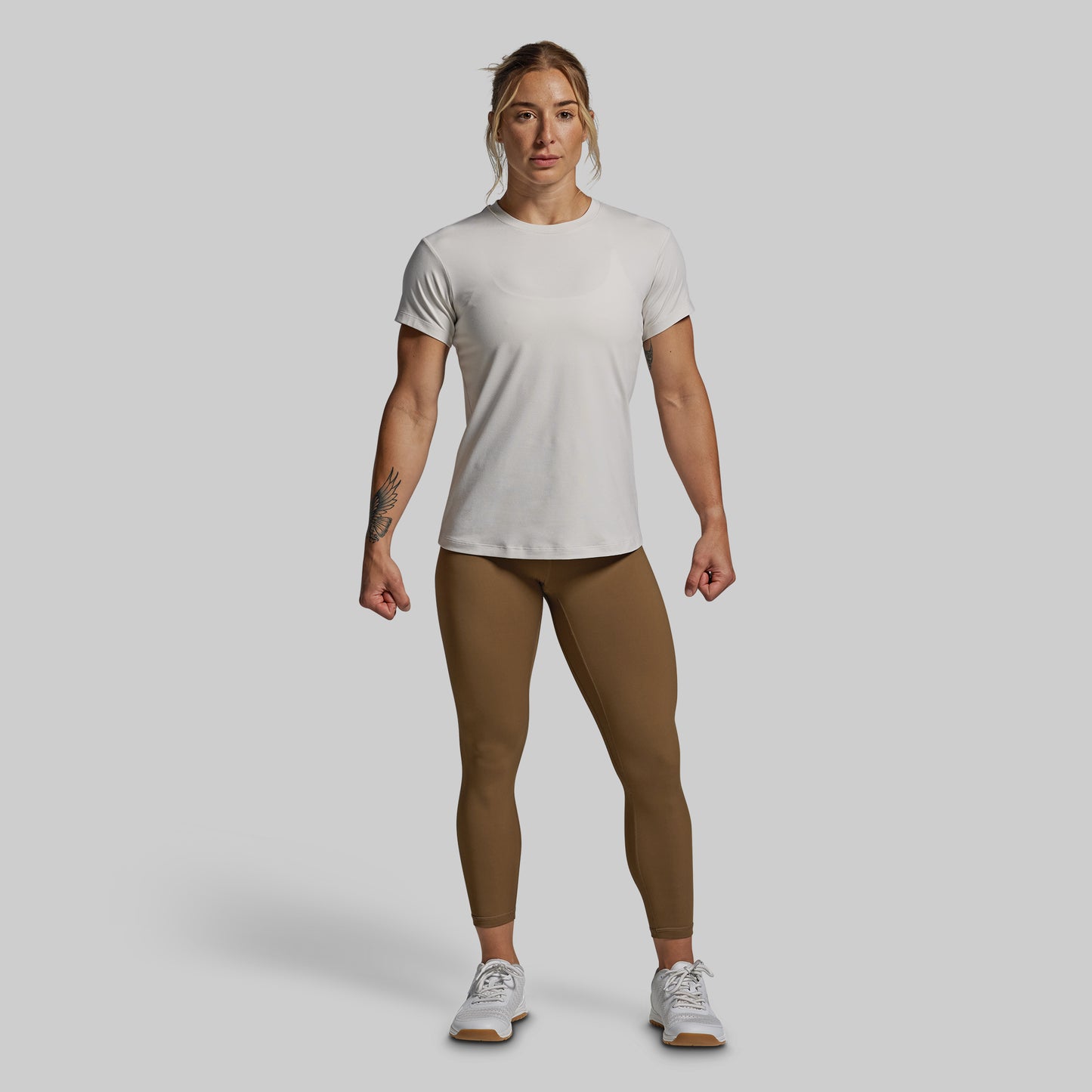 Person wearing a white t-shirt and brown leggings on a plain background