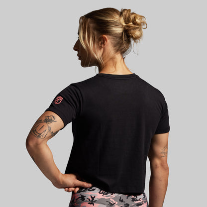 Person wearing a black t-shirt with a small pink logo on a gray background