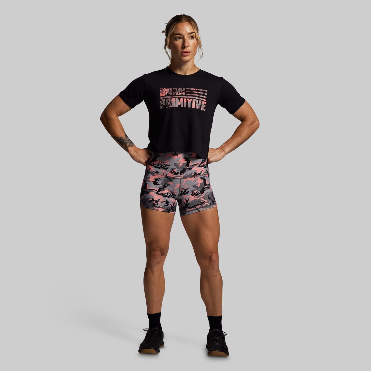 Woman wearing a black t-shirt and pink camouflage shorts on a gray background