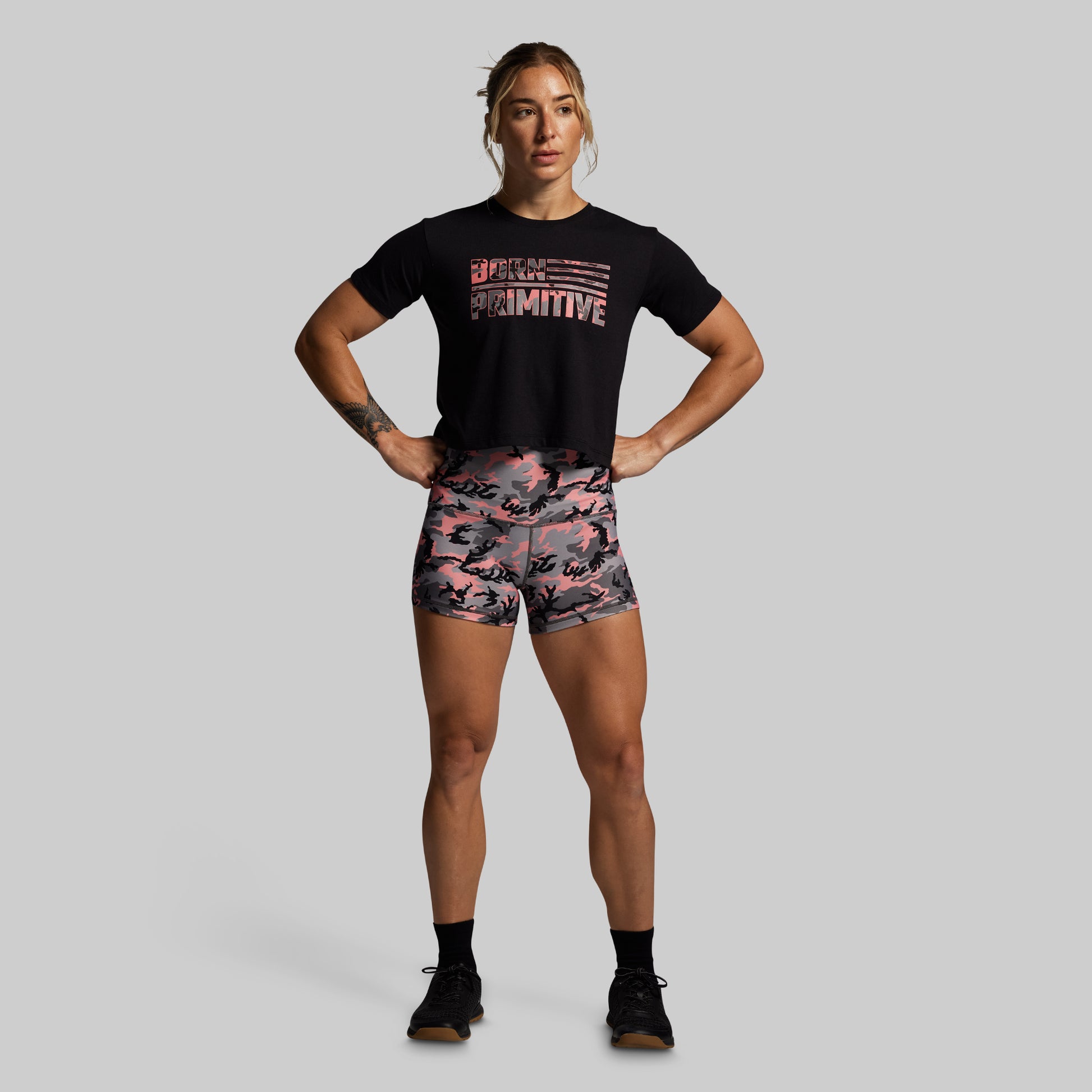Woman wearing a black t-shirt and pink camouflage shorts on a gray background