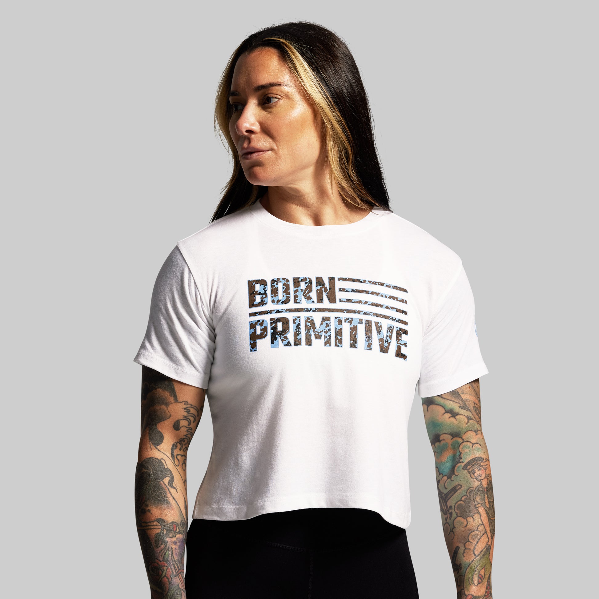Person wearing a white t-shirt with 'BORN PRIMITIVE' text on a gray background
