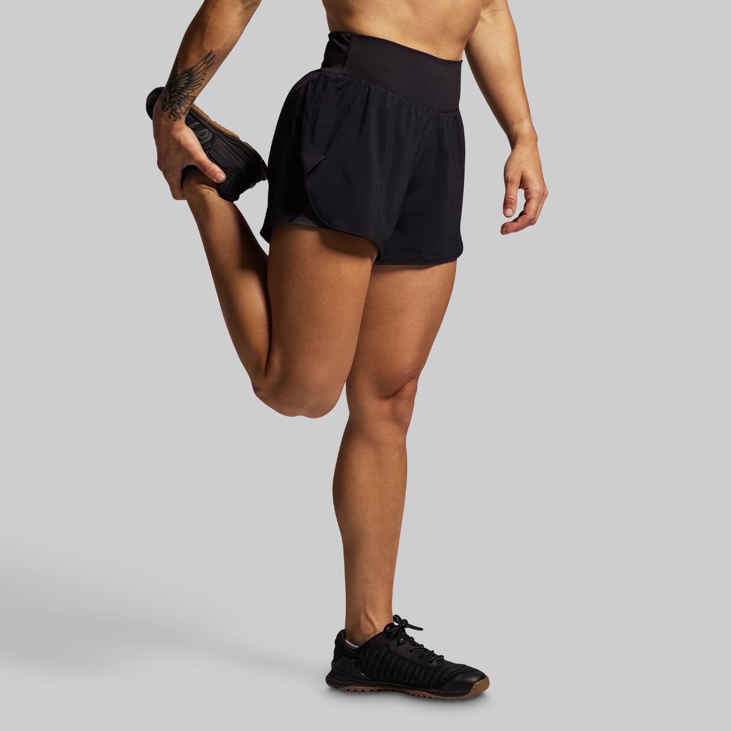 Person wearing black athletic shorts and shoes on a gray background