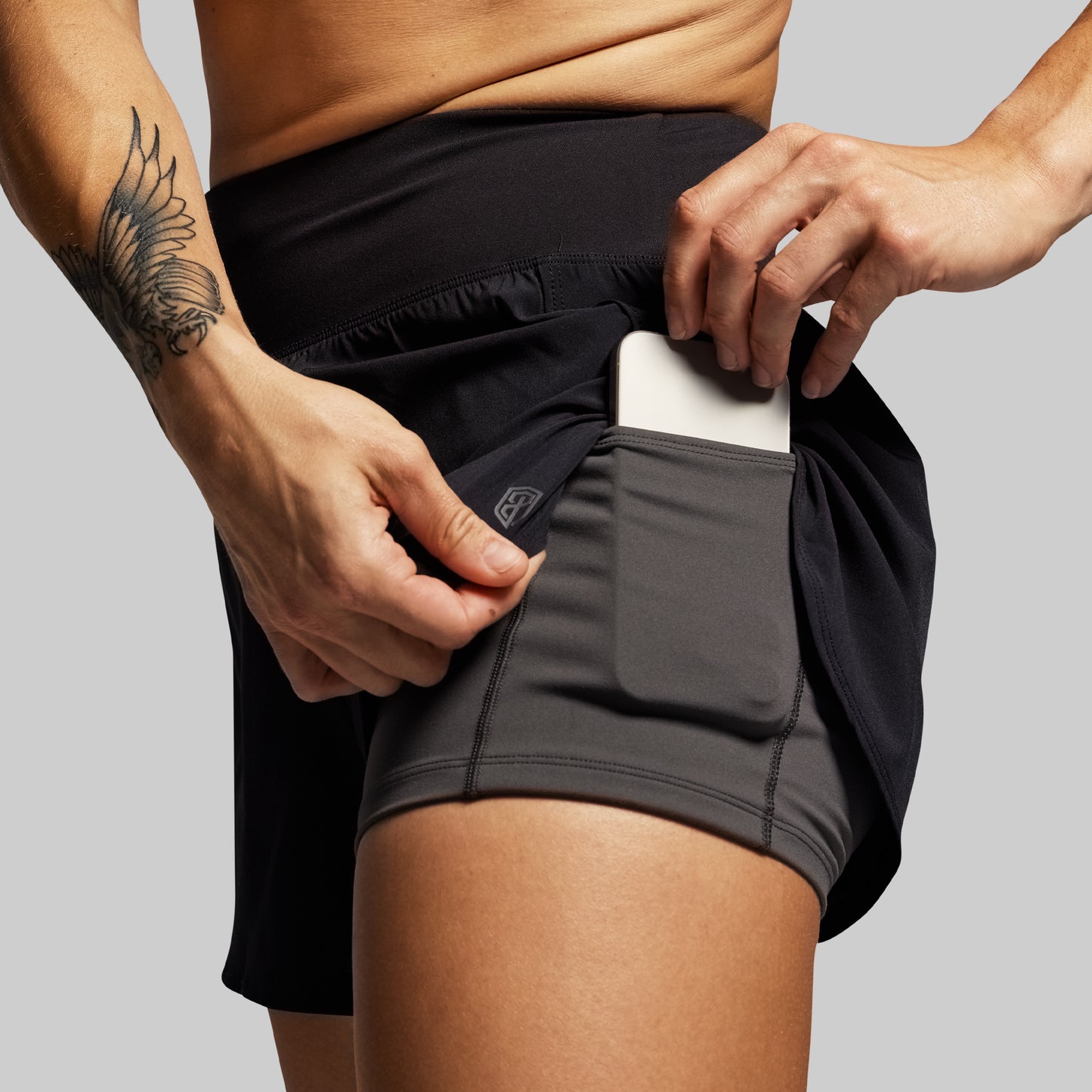 Person wearing black athletic shorts with a pocket, holding a phone.