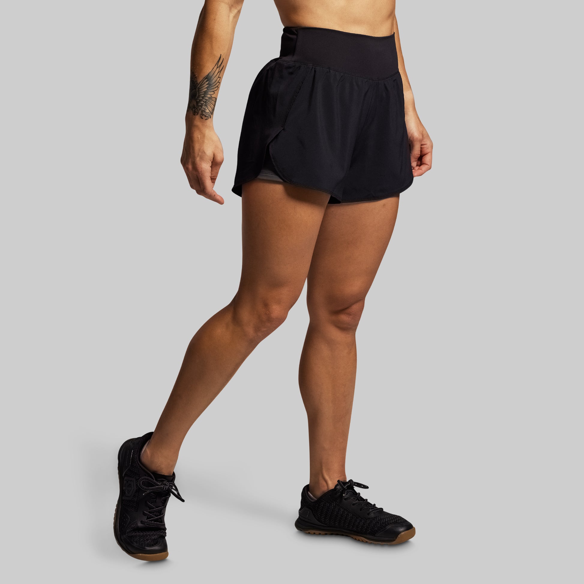 Person wearing black athletic shorts and black sneakers on a gray background