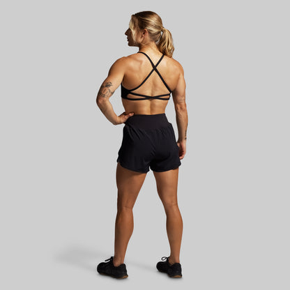 Woman wearing a black sports bra and shorts on a gray background