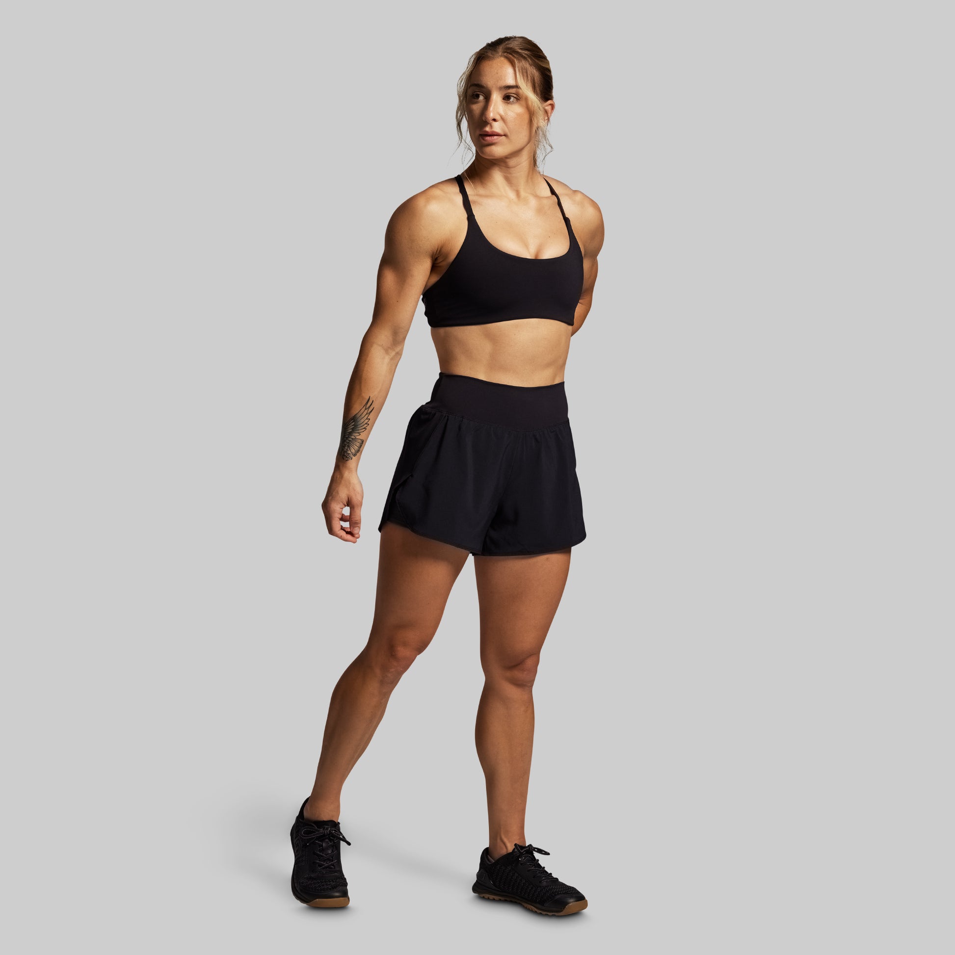 Woman wearing a black sports bra and shorts on a gray background