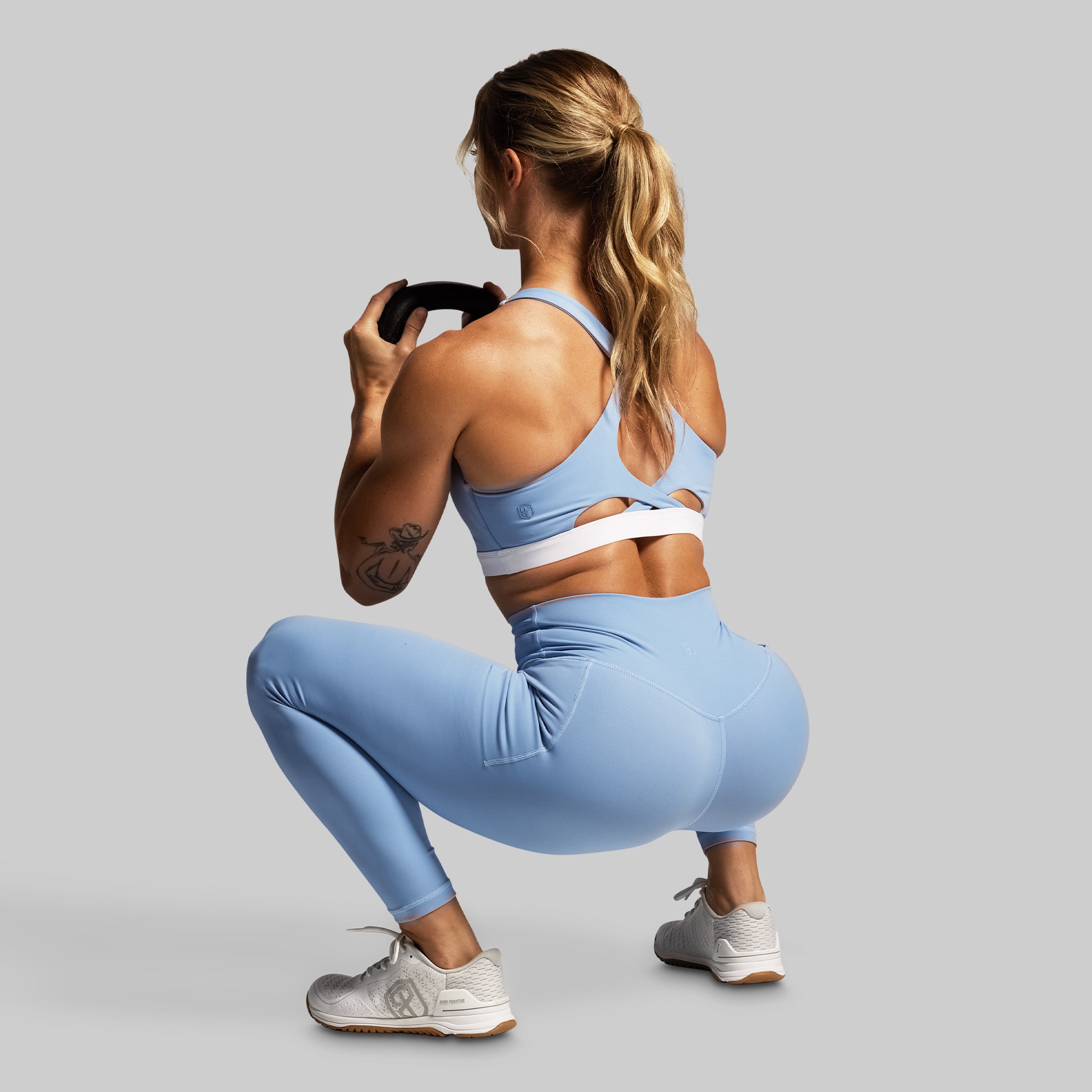 Woman in blue athletic wear performing a squat against a gray background