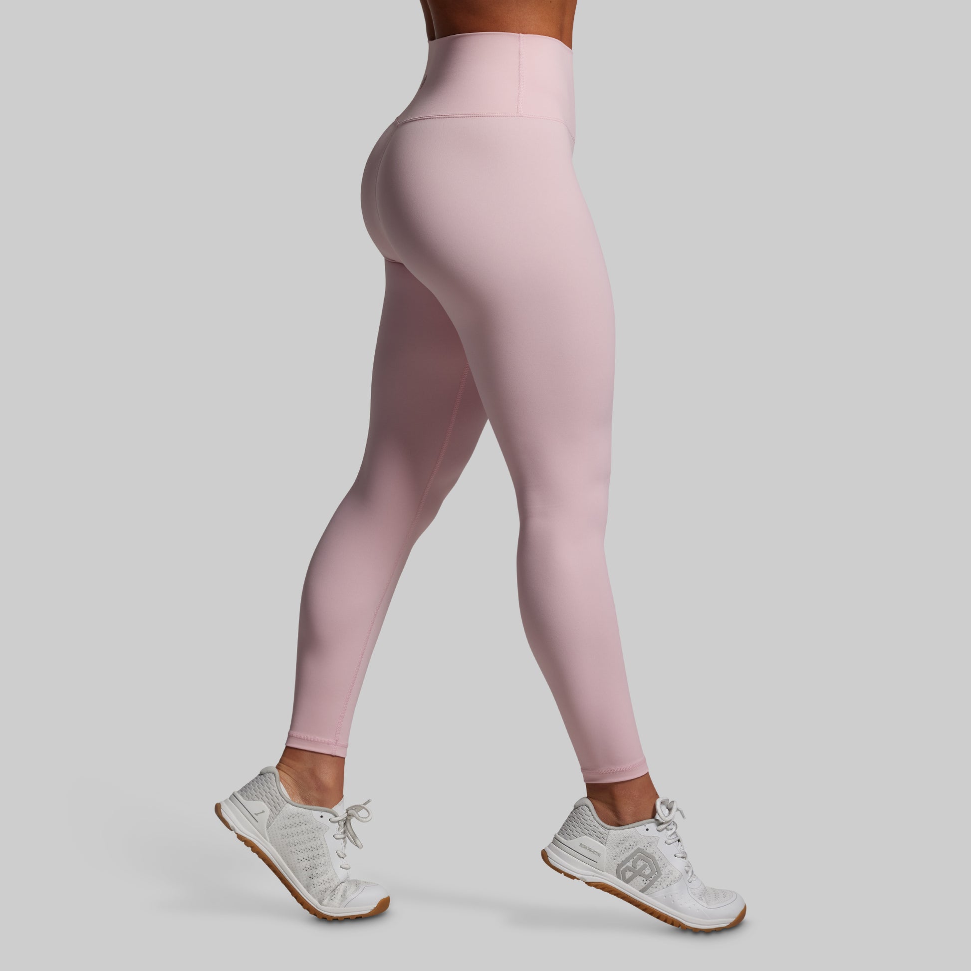 Person wearing pink leggings and white sneakers on a light gray background