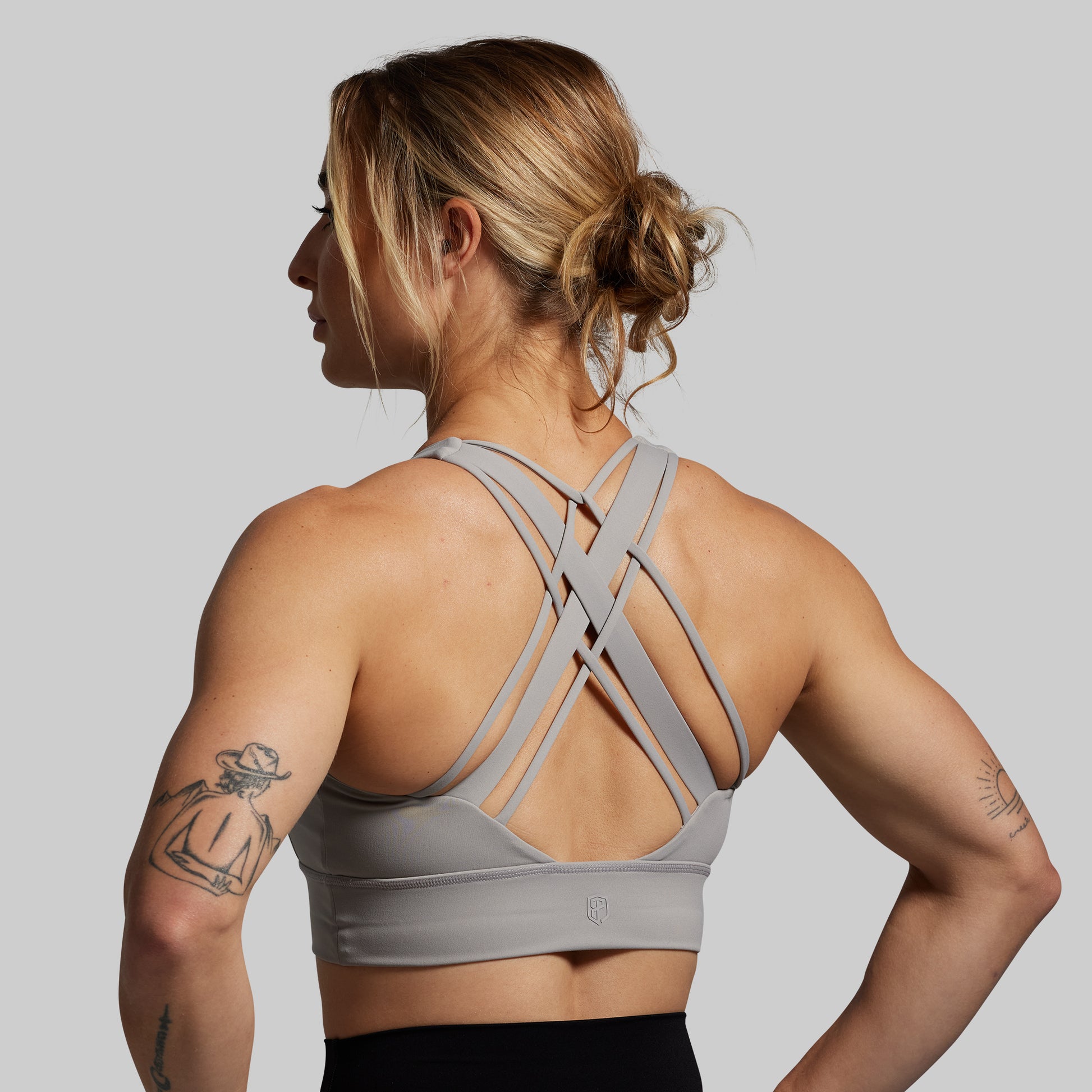 Woman wearing a gray sports bra with criss-cross straps on a plain background