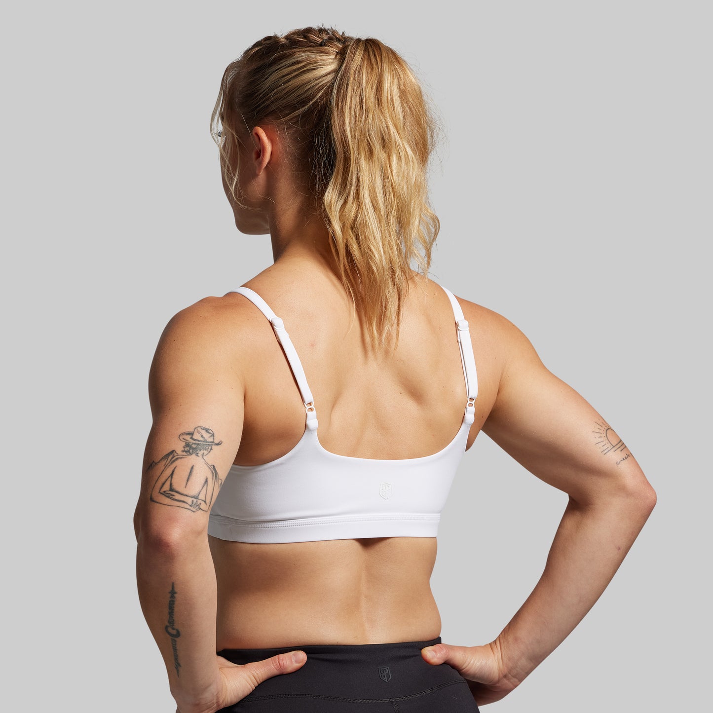 A person wearing a white sports bra with a scoop neckline and thin straps, facing away from the camera.