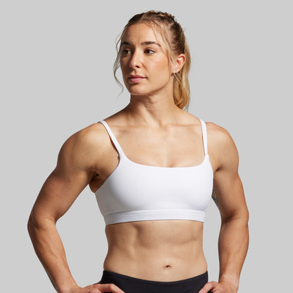 Woman wearing a white sports bra and black leggings on a gray background