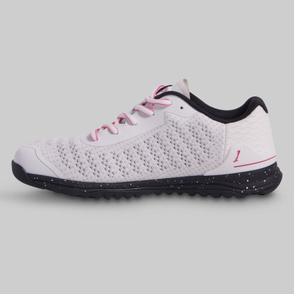White athletic shoe with black sole and pink laces on a gray background