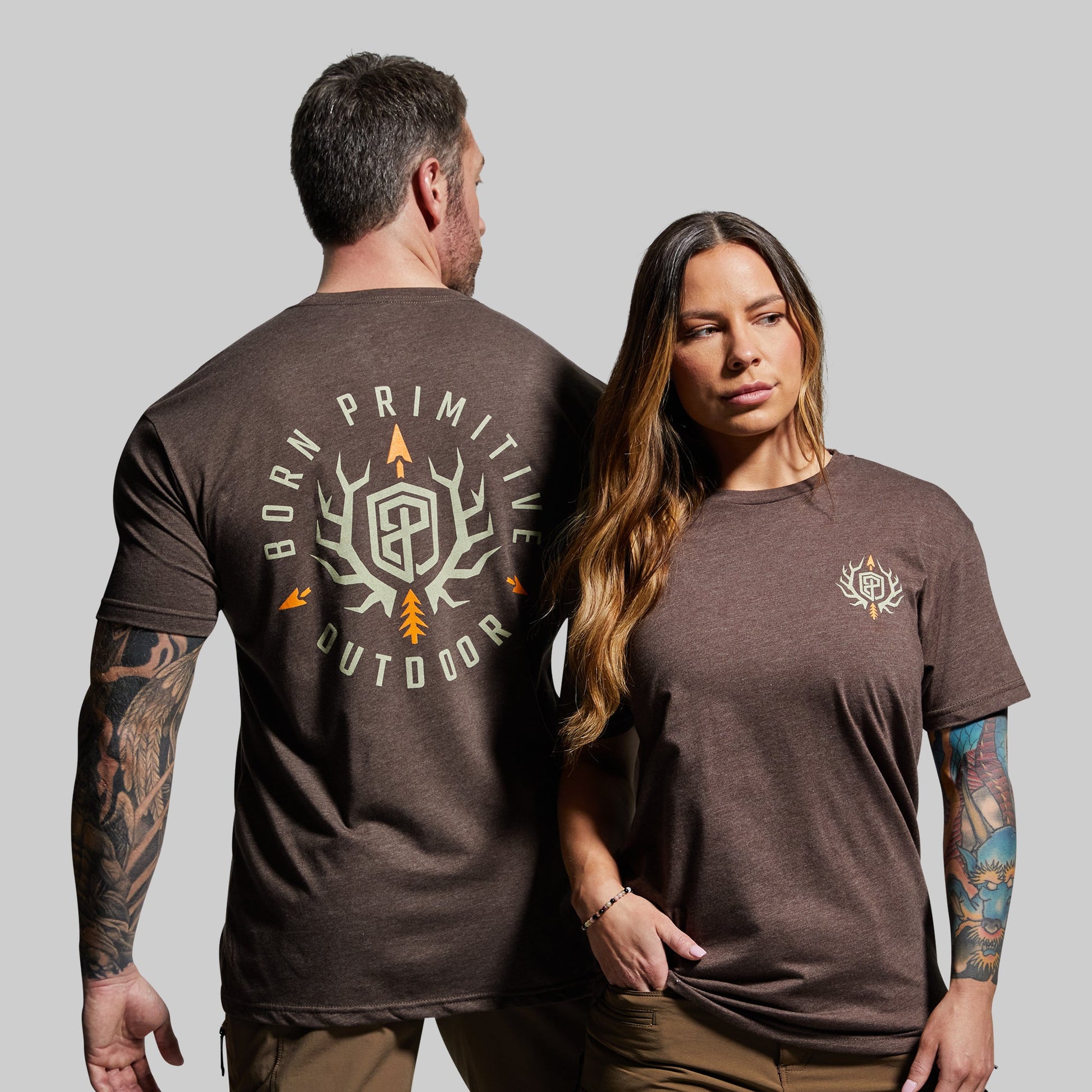 Man and woman wearing brown t-shirts with a visible brand logo on a gray background