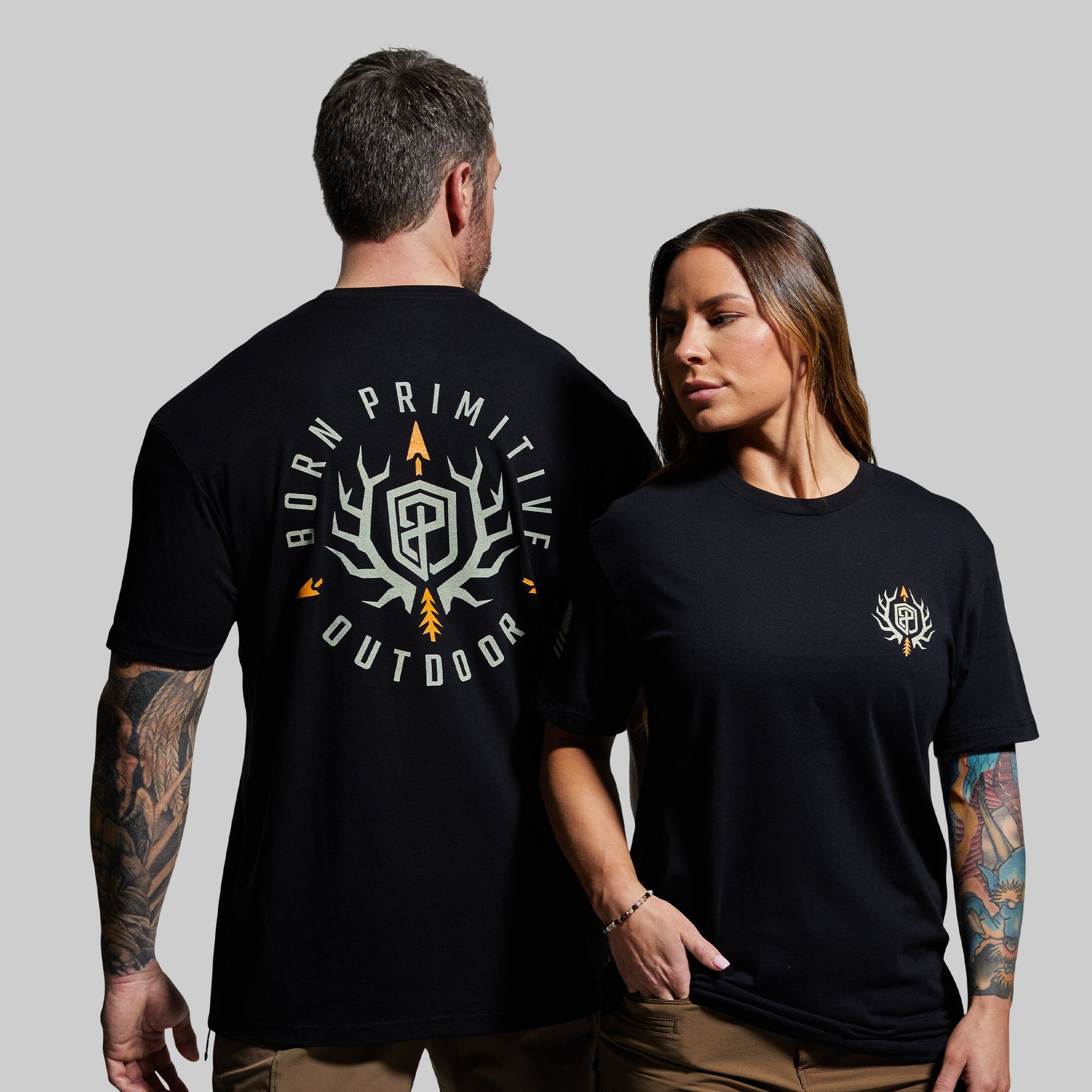 Two people wearing black t-shirts with logos on a gray background