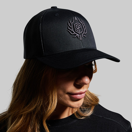 Person wearing a black cap with a logo on a gray background