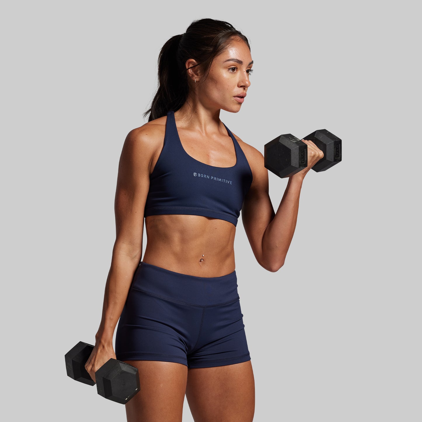 Woman in navy athletic wear lifting dumbbells against a gray background