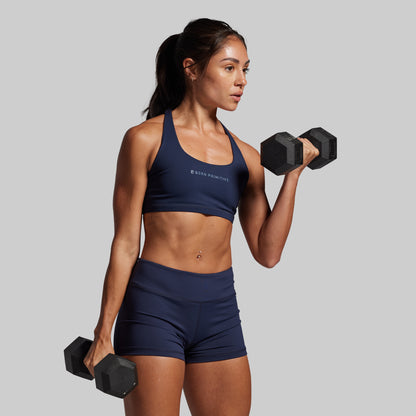 Woman in navy athletic wear lifting dumbbells against a gray background