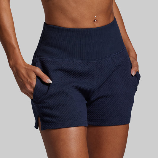 Navy blue shorts worn by a person on a gray background