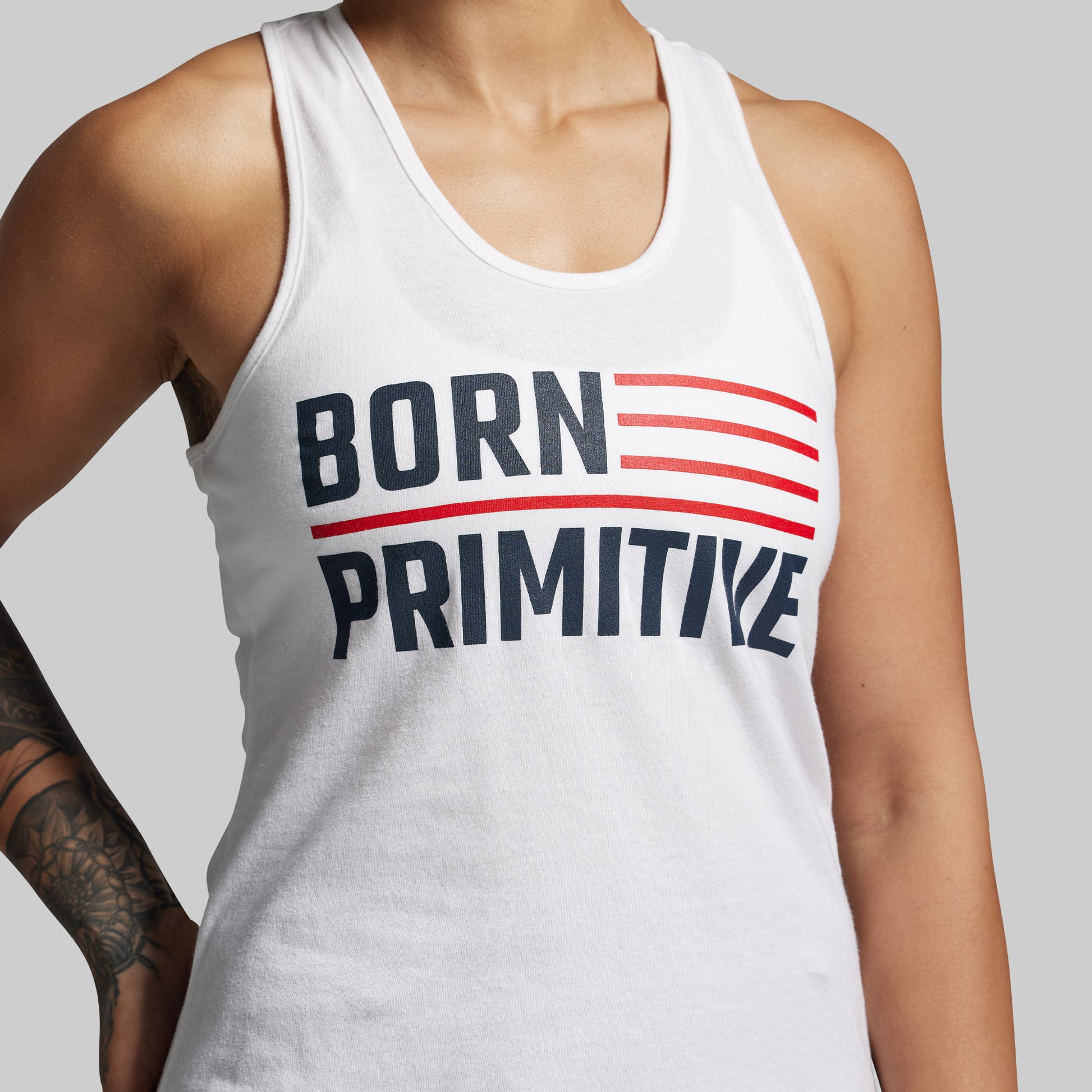 Person wearing a white tank top with 'BORN PRIMITIVE' text design.