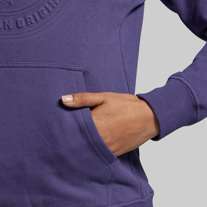 Person wearing a purple hoodie with a hand in the pocket against a gray background