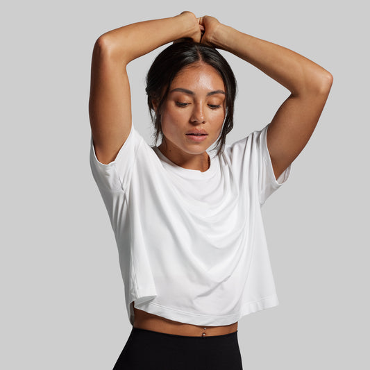 Woman wearing a white crop top and black pants against a gray background