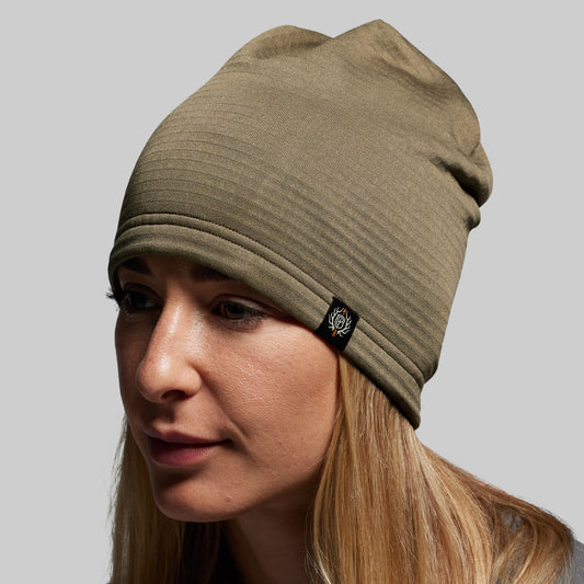 Woman wearing a green beanie with a brand logo on a gray background