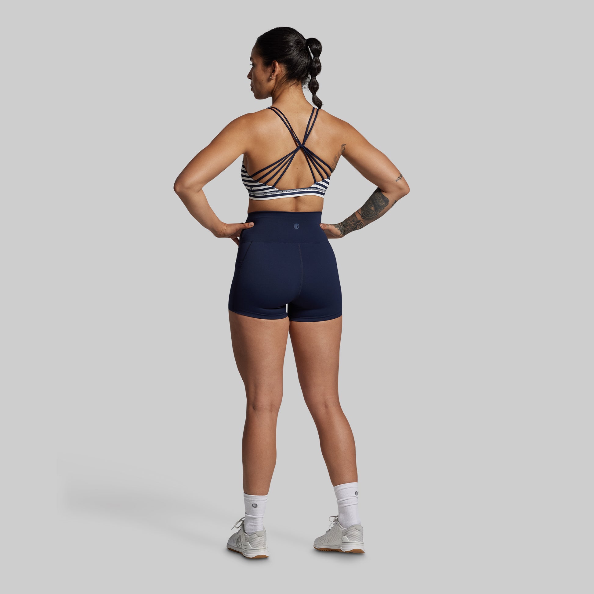 Woman wearing a sports bra and shorts on a plain background