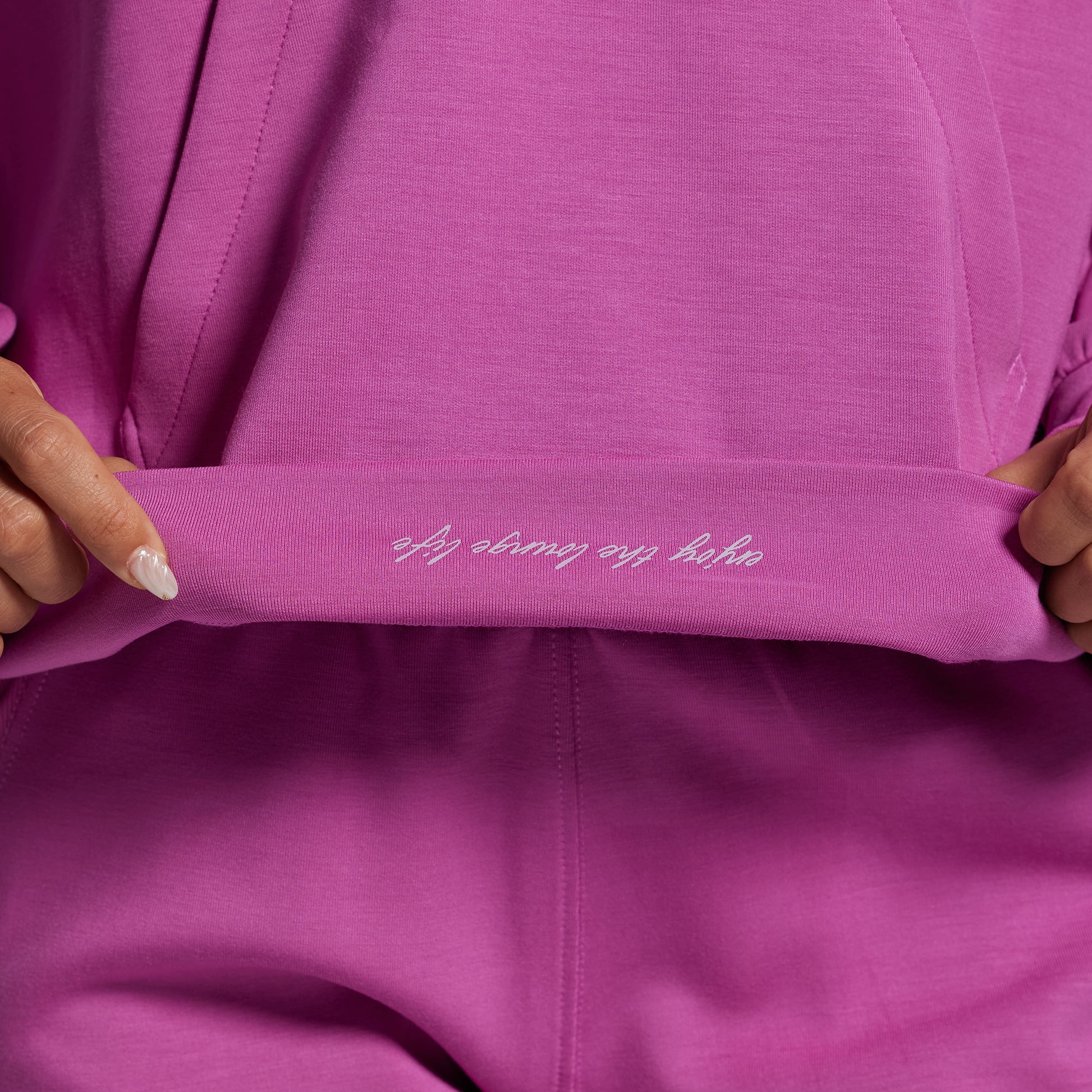 Close-up of a pink garment with text on it, held by hands.