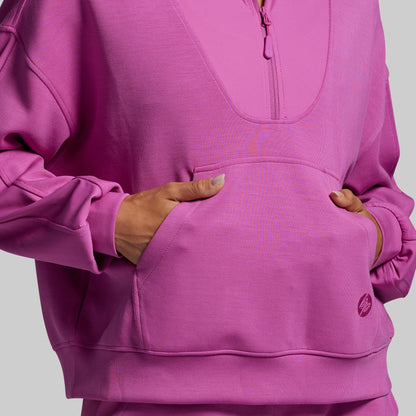 Person wearing a pink pullover with hands in pockets on a gray background