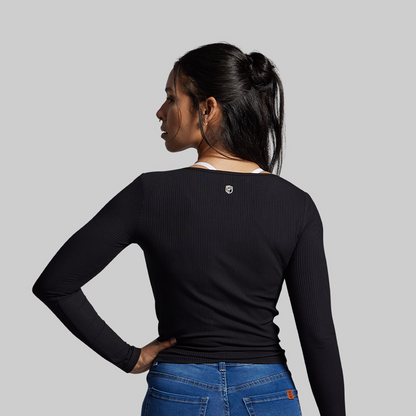 Woman wearing a black long-sleeve top and blue jeans on a gray background