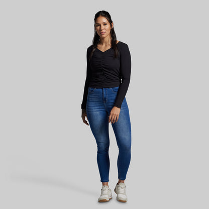 Woman wearing blue jeans and a black long-sleeve top on a gray background