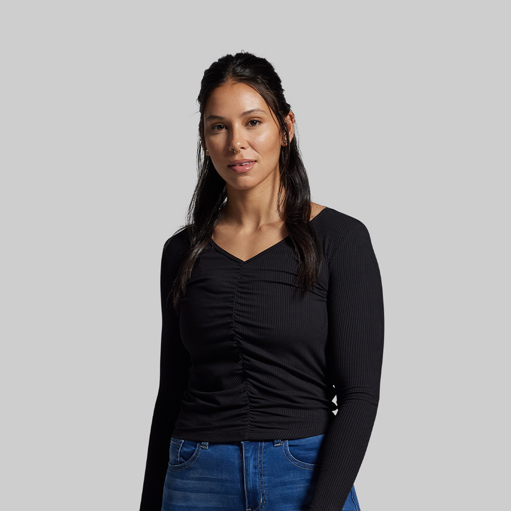 Woman wearing a black long-sleeve top and blue jeans against a gray background