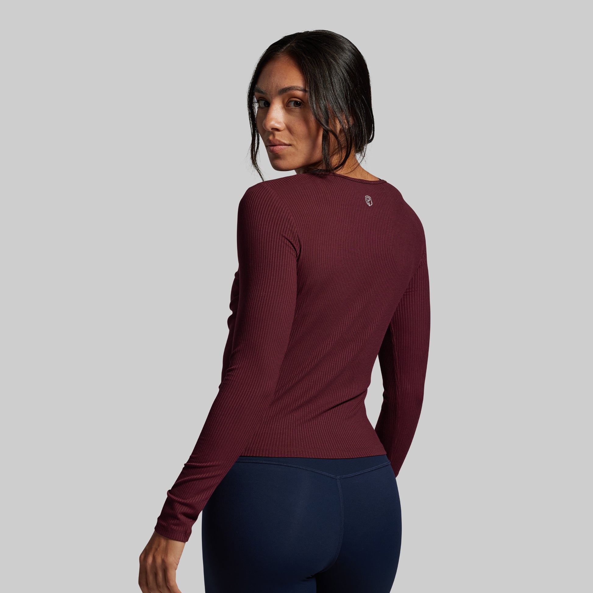Woman wearing a maroon long-sleeve top and navy leggings on a gray background
