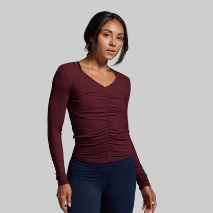 Woman wearing a maroon long-sleeve top and navy leggings on a gray background
