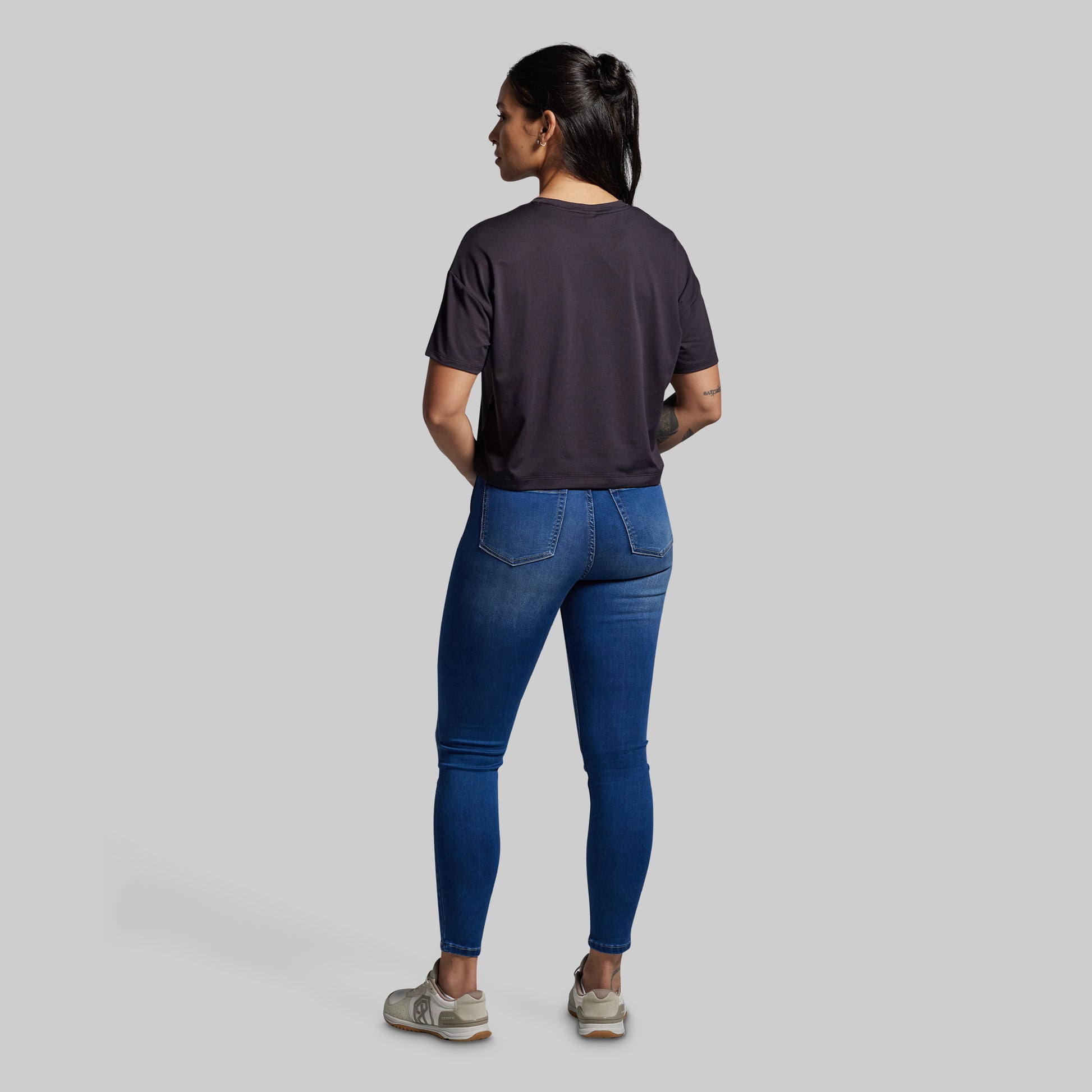 Person wearing a dark t-shirt and blue jeans on a gray background